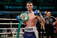 a boxer holding a belt in front of a boxing ring