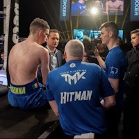 a group of boxers are sitting on the floor in front of a boxing ring