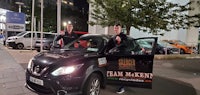 two men standing next to a car at night