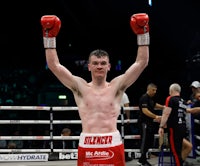 a boxer raises his arms in the air after winning a boxing match