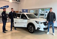 three men standing next to a white suv in a showroom